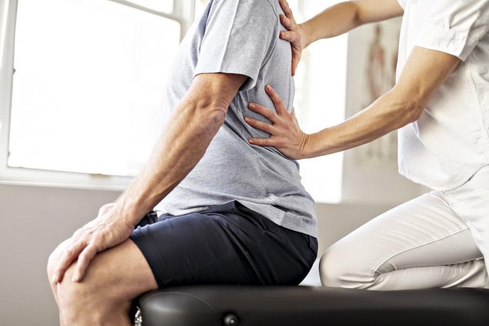 Aero Performance physical therapist assessing a seated patient’s lower back during a back pain evaluation in the Coralville, Iowa clinic