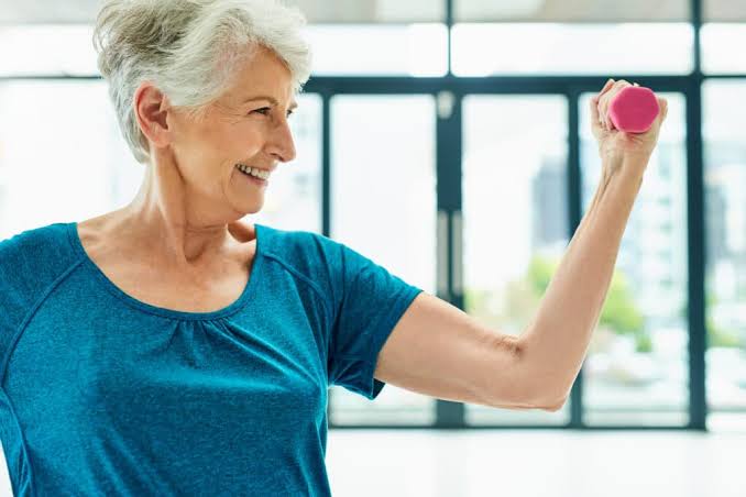 Older adult patient smiling while lifting a light dumbbell as part of a bone-health strength training program at Aero Performance in Coralville, Iowa