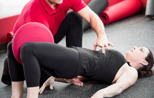 Aero Performance physical therapist cueing a patient’s pelvis during a bridge exercise with a stability ball between her knees in the Coralville, Iowa clinic